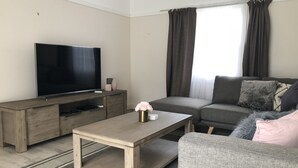 Una sala de estar moderna con un televisor de pantalla plana, una mesa de centro de madera, un sofá gris y un sillón gris.