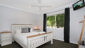 A bedroom with a white bed, a nightstand, a bedside table, a ceiling fan, a window with curtains, and a painting on the wall. - Marshmallow Retreat (Bright)