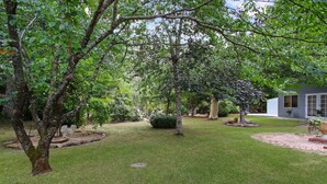 A well-maintained garden with various trees and shrubs, a brick pathway, and a house in the background. - Marshmallow Retreat (Bright)
