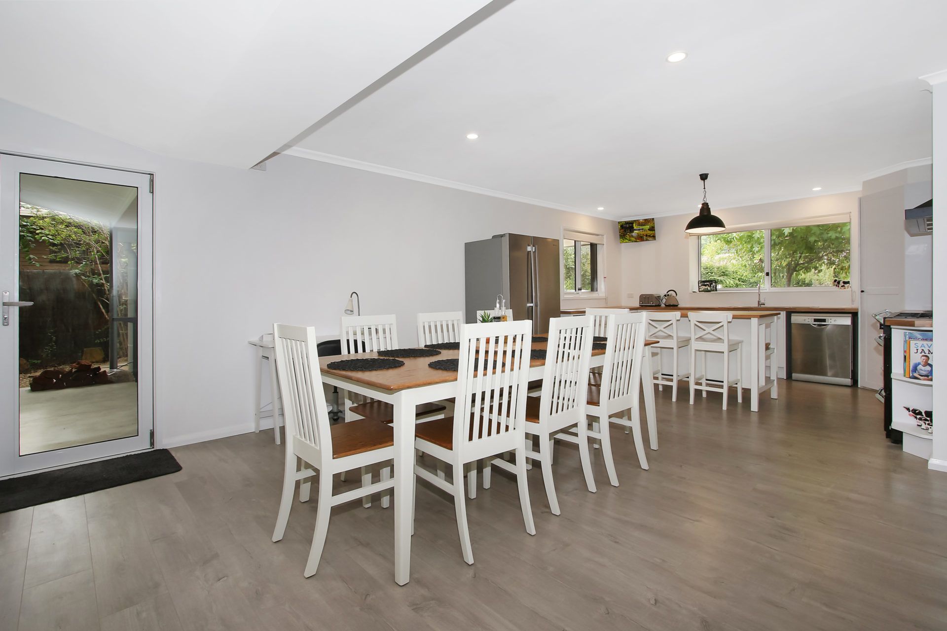 A modern kitchen with white cabinetry, a central island, and a dining area with white chairs and a wooden table.