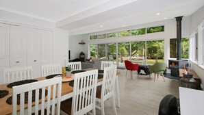 A modern kitchen with white cabinetry, a dining area with white chairs, and a large sliding glass door leading to a garden. - Marshmallow Retreat (Bright)