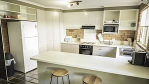 A modern kitchen with white cabinets, a central island with stools, a brick backsplash, and a microwave. - Monty's On Lumley Drive (Bright)