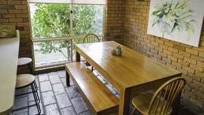 A wooden dining table with benches, a brick wall, and a window with a view of trees. - Monty's On Lumley Drive (Bright)