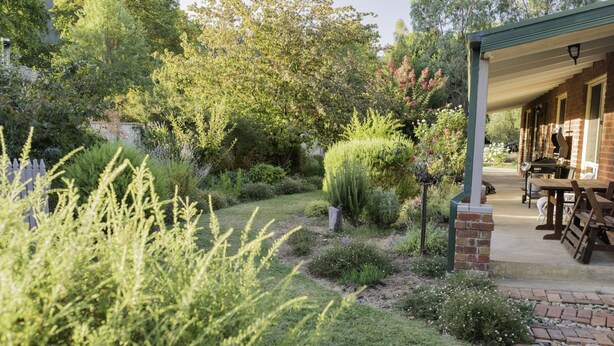 A garden with a patio area featuring a brick wall, a wooden table, and a covered seating area. - Monty's On Lumley Drive (Bright)