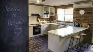 A kitchen with a chalkboard wall displaying "Welcome to Bright," a brick wall, a window with blinds, and a coffee station. - Monty's On Lumley Drive (Bright)
