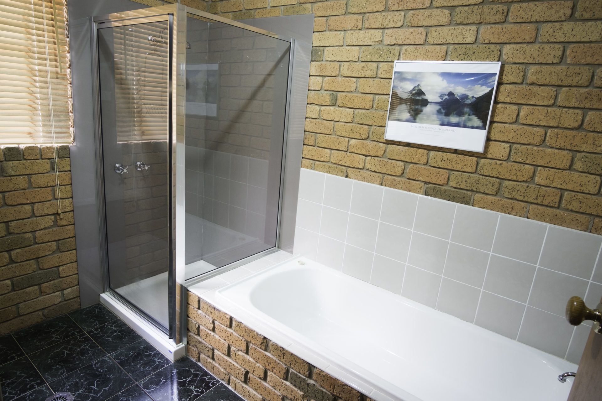 A bathroom with a glass-enclosed shower, a white bathtub, and a brick wall.