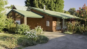 A brick building with a green roof, a covered porch, and a garden with white flowers. - Monty's On Lumley Drive (Bright)