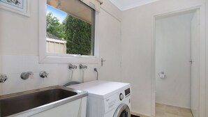 Un cuarto de lavandería con lavadora, lavamanos y ventana con vista a un jardín.