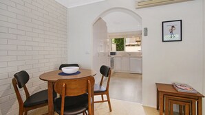 Una cocina compacta con armarios blancos, un microondas y un lavavajillas. Hay un pequeño comedor con una mesa redonda y dos sillas.
