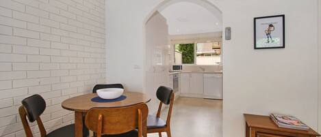 A compact kitchen with white cabinets, a microwave, and a dishwasher. There is a small dining area with a round table and two chairs.