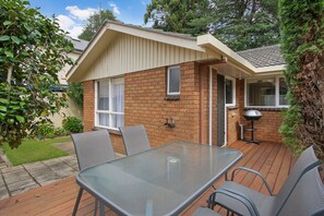 A small brick house with a glass table and chairs, a barbecue grill, and a garden with a lawn and trees. - Woody's In Central Bright (Bright)