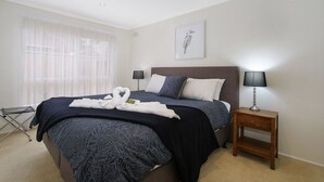 Habitación de hotel impecable con una cama, dos mesitas de noche, una ventana con cortinas translúcidas y una obra de arte colgada en la pared.