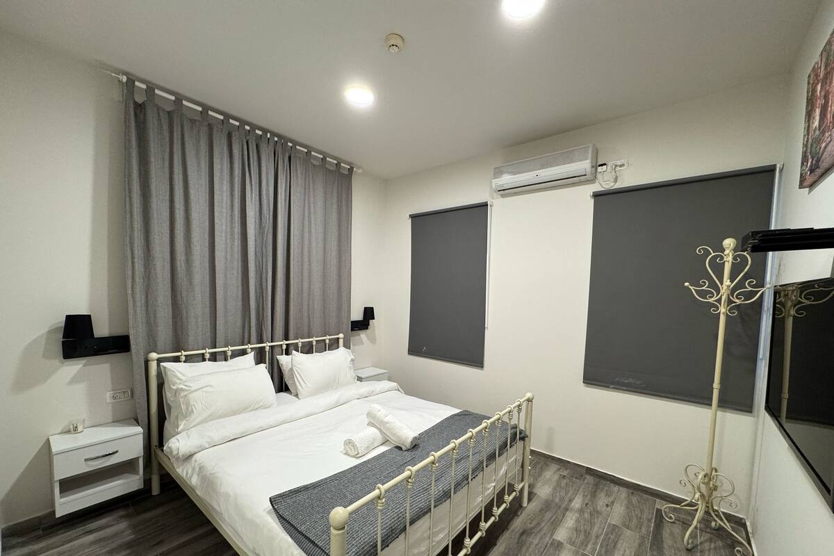 A modern bedroom with a bed, bedside tables, curtains, an air conditioning unit, and a coat stand.