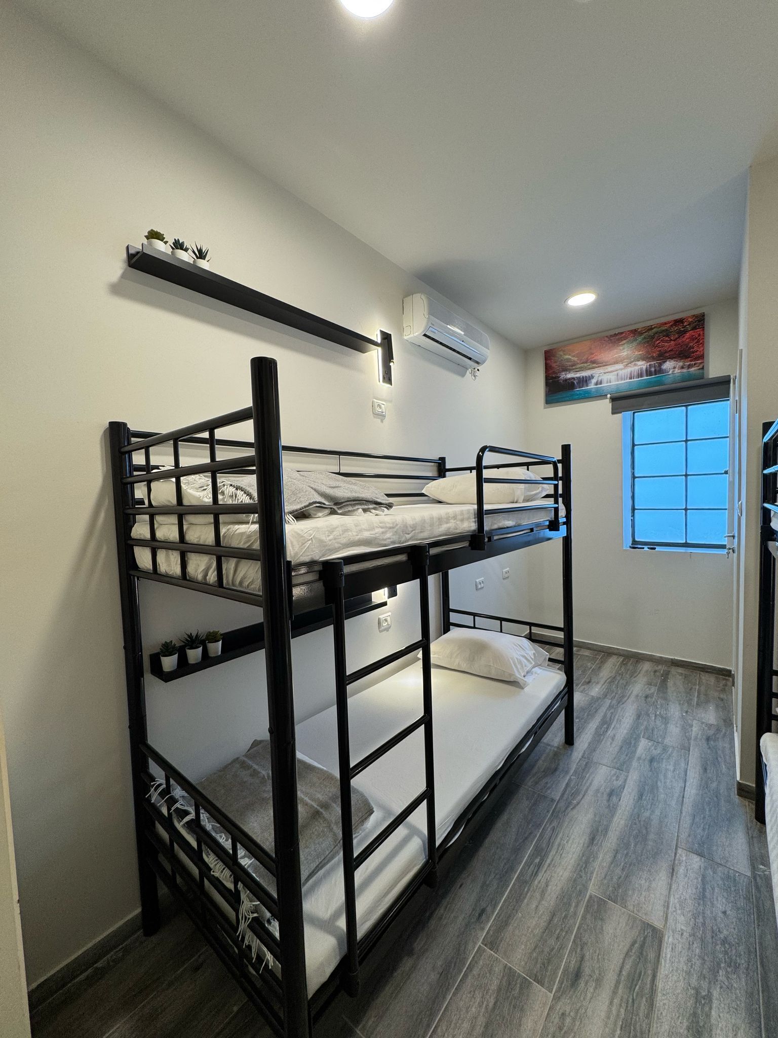 A bunk bed room with a window, an air conditioning unit, and a shelf with plants.