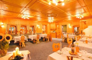 A warmly lit dining area with wooden paneling, tables set for dining, and decorative elements like candles and sunflowers.