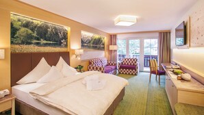 Quarto de hotel com cama, escrivaninha, cadeira e varanda com vista para áreas verdes.