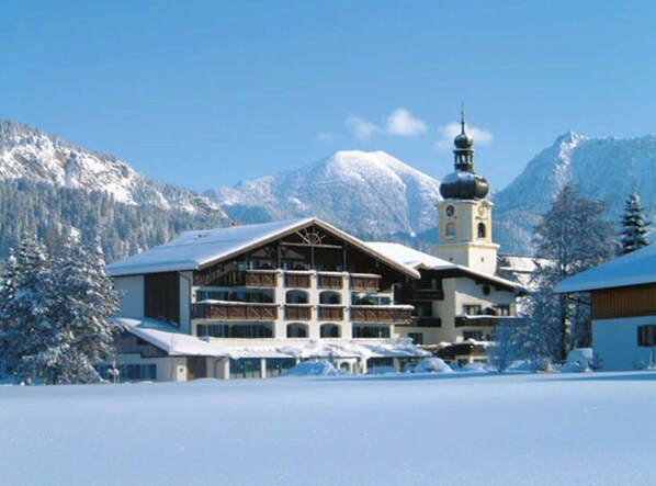 A hotel with a snow-covered roof, a bell tower, and a mountain backdrop.