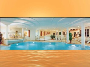 An indoor swimming pool with a sunlit ceiling, a seating area with chairs, and a staircase leading to an upper level.