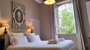 Un lit bien fait, avec du linge de lit blanc et des oreillers, deux lampes de chevet, une œuvre d’art encadrée au-dessus du lit et une fenêtre donnant sur la forêt.