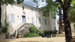 Un bâtiment doté d’un escalier menant à une porte, entouré d’arbres et d’un jardin.