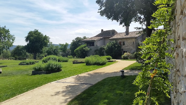 Une maison en pierre avec un toit en tuiles, entourée de jardins bien entretenus et bordée d’un chemin de gravier.