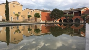 Une cour avec un bassin d’eau miroitante, des bâtiments aux toits de tuiles et des arbres.