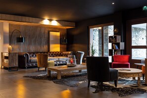 Un salon moderne avec un canapé en cuir, une table basse, un fauteuil rouge et une bibliothèque.