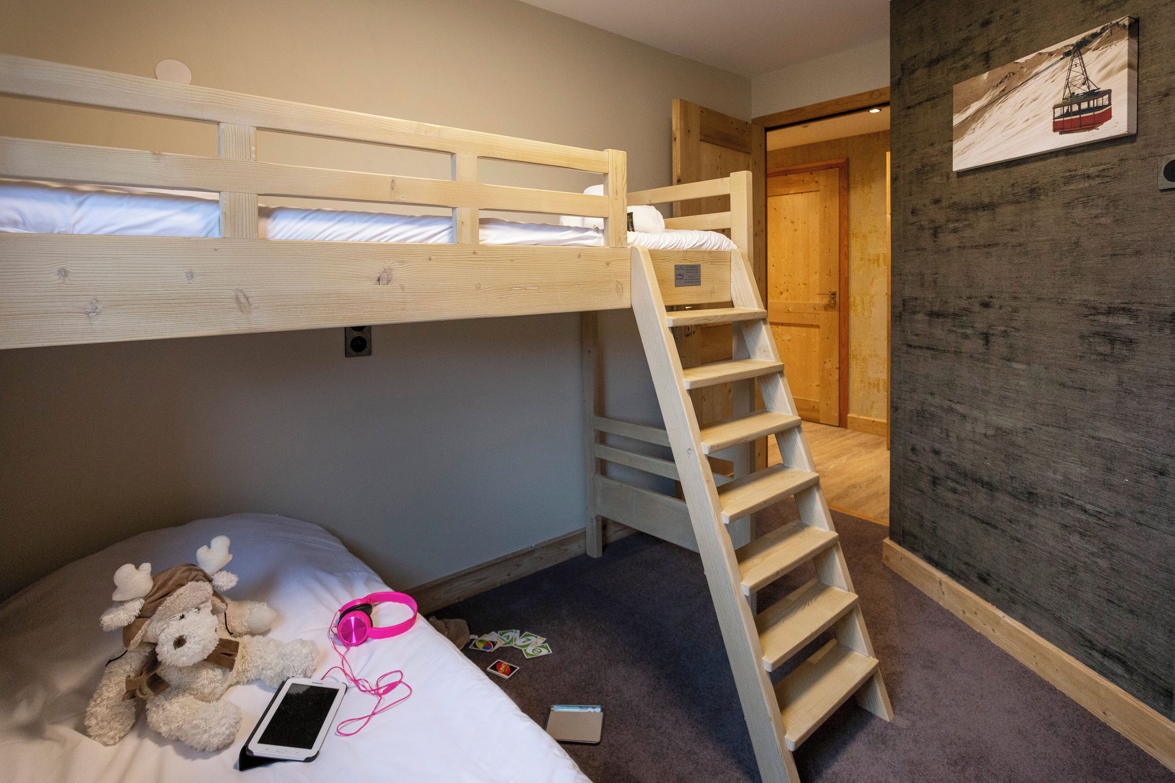 A bunk bed with a wooden ladder, a plush toy, and a smartphone on the lower bed.