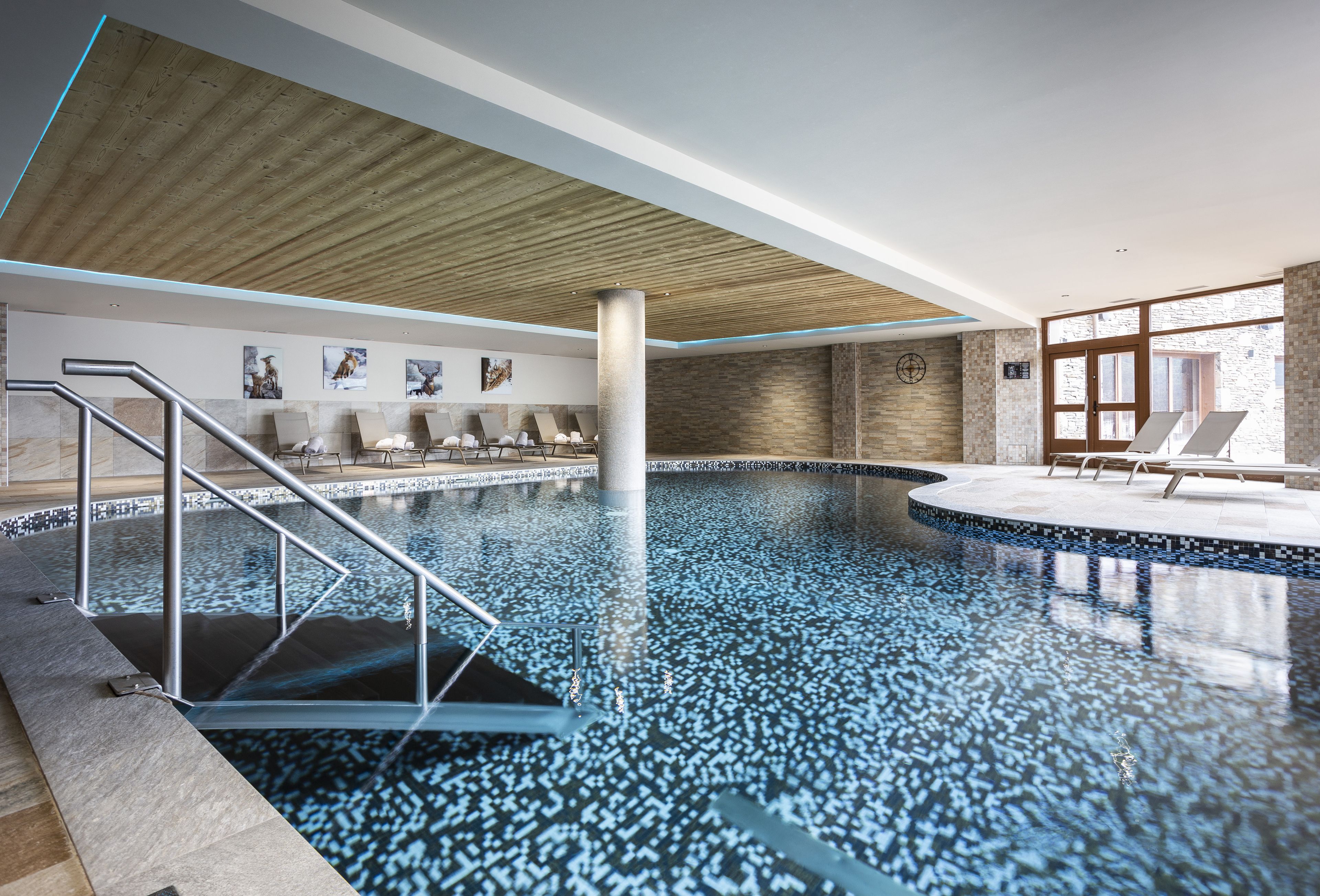 An indoor swimming pool with a wooden ceiling, tiled walls, and lounge chairs.