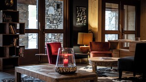 Une pièce chaleureuse avec un mur en pierre, un fauteuil rouge, une table en bois avec une bougie et une lampe.