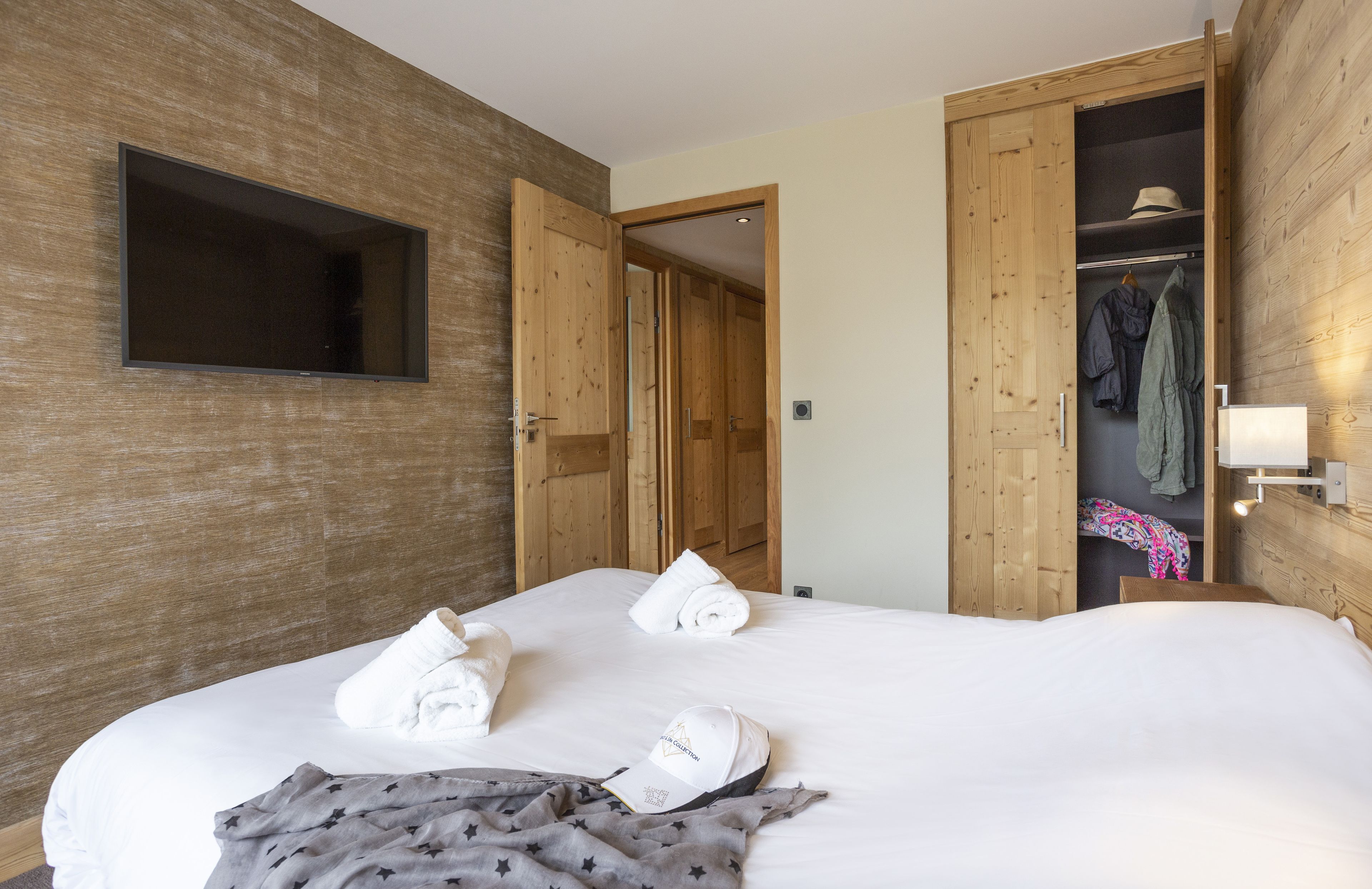Ett hotellrum med en stor säng, en garderob i trä och en tv som är monterad på väggen.