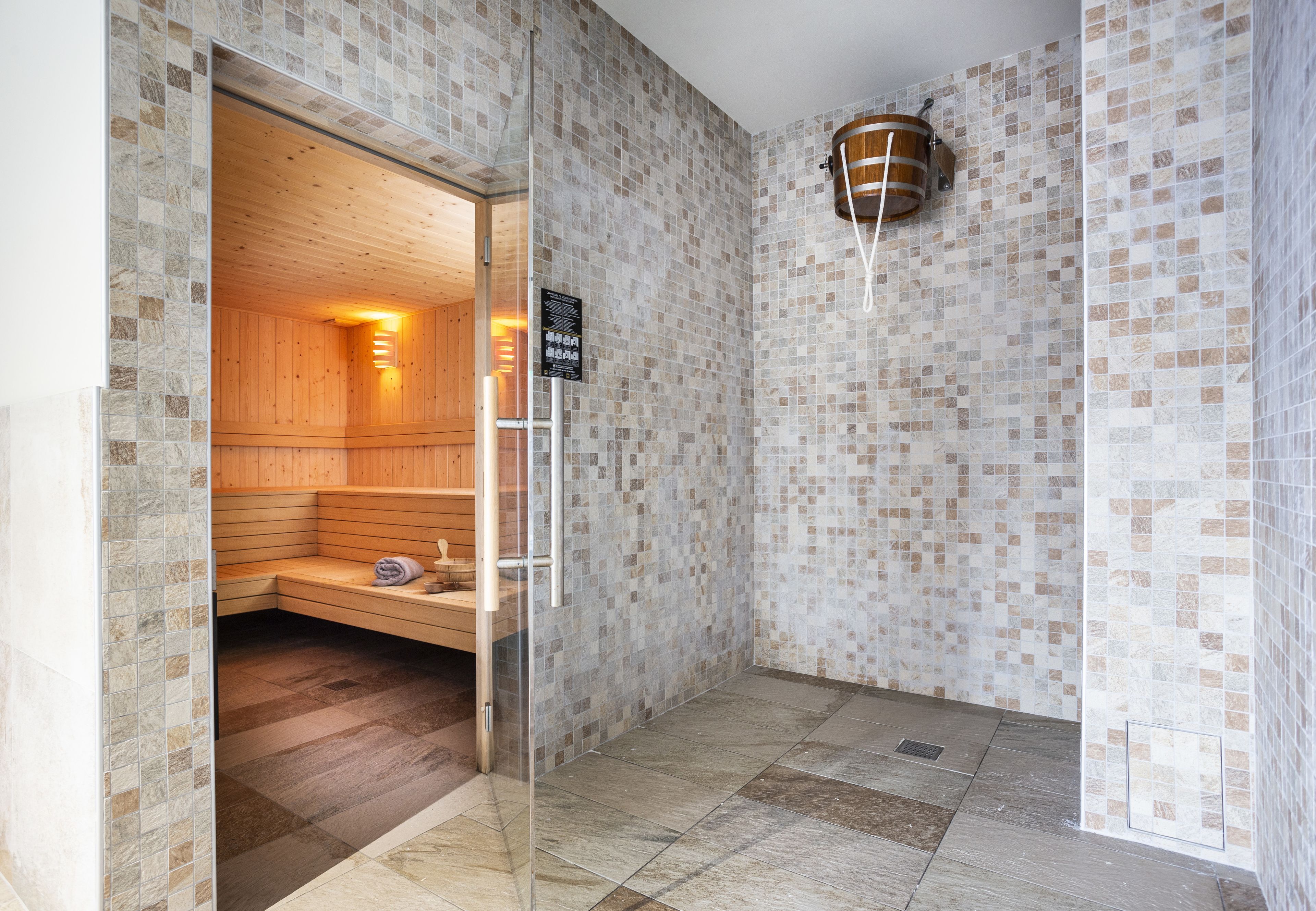 A sauna room with a wooden bench and a glass door leading to a tiled area.