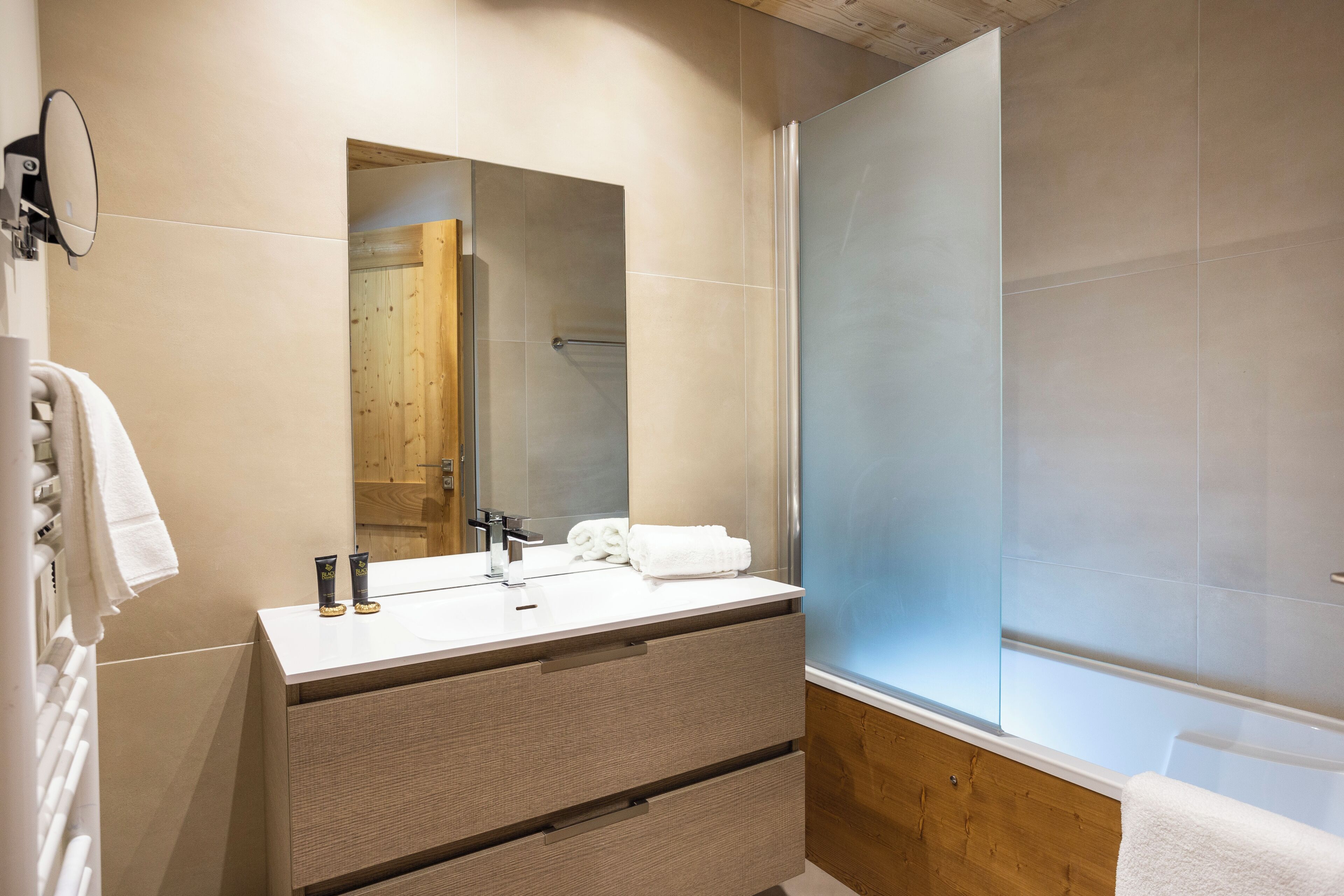 A modern bathroom with a large mirror, a sink with two faucets, a wooden vanity, and a glass shower enclosure.
