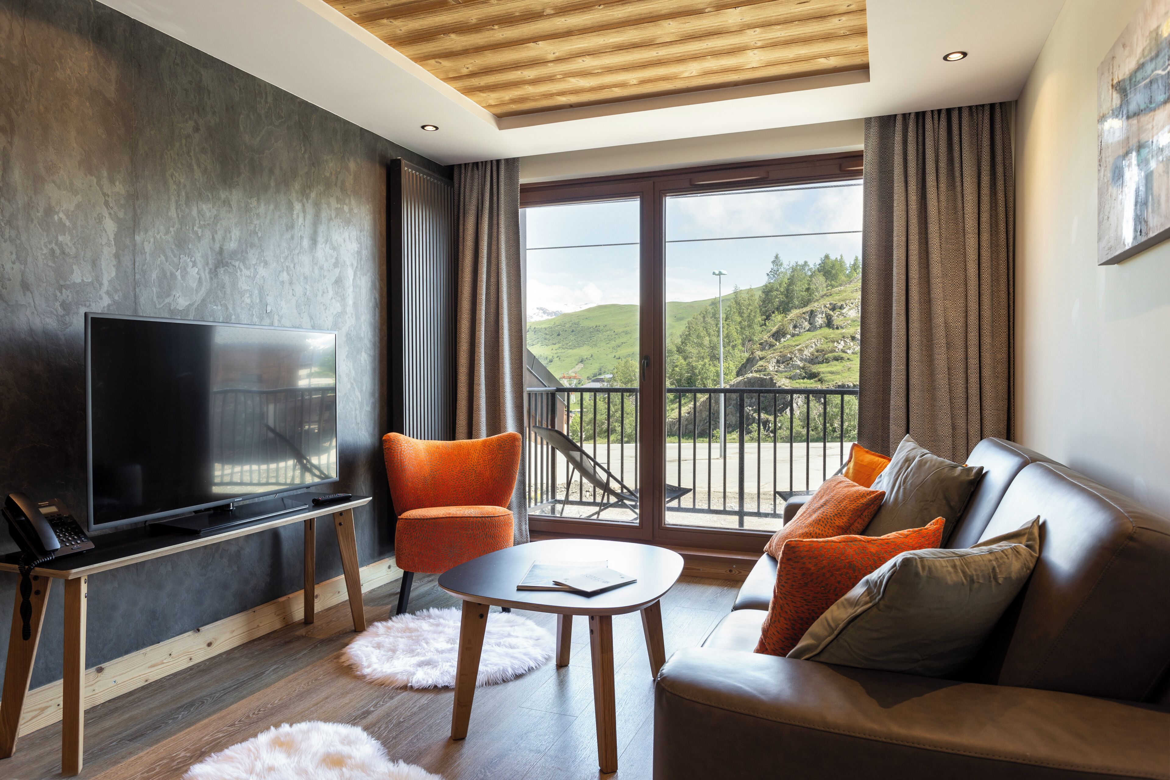 Een moderne woonkamer met een flatscreen televisie, een bank, een stoel, een salontafel en een balkon met uitzicht op de heuvels.