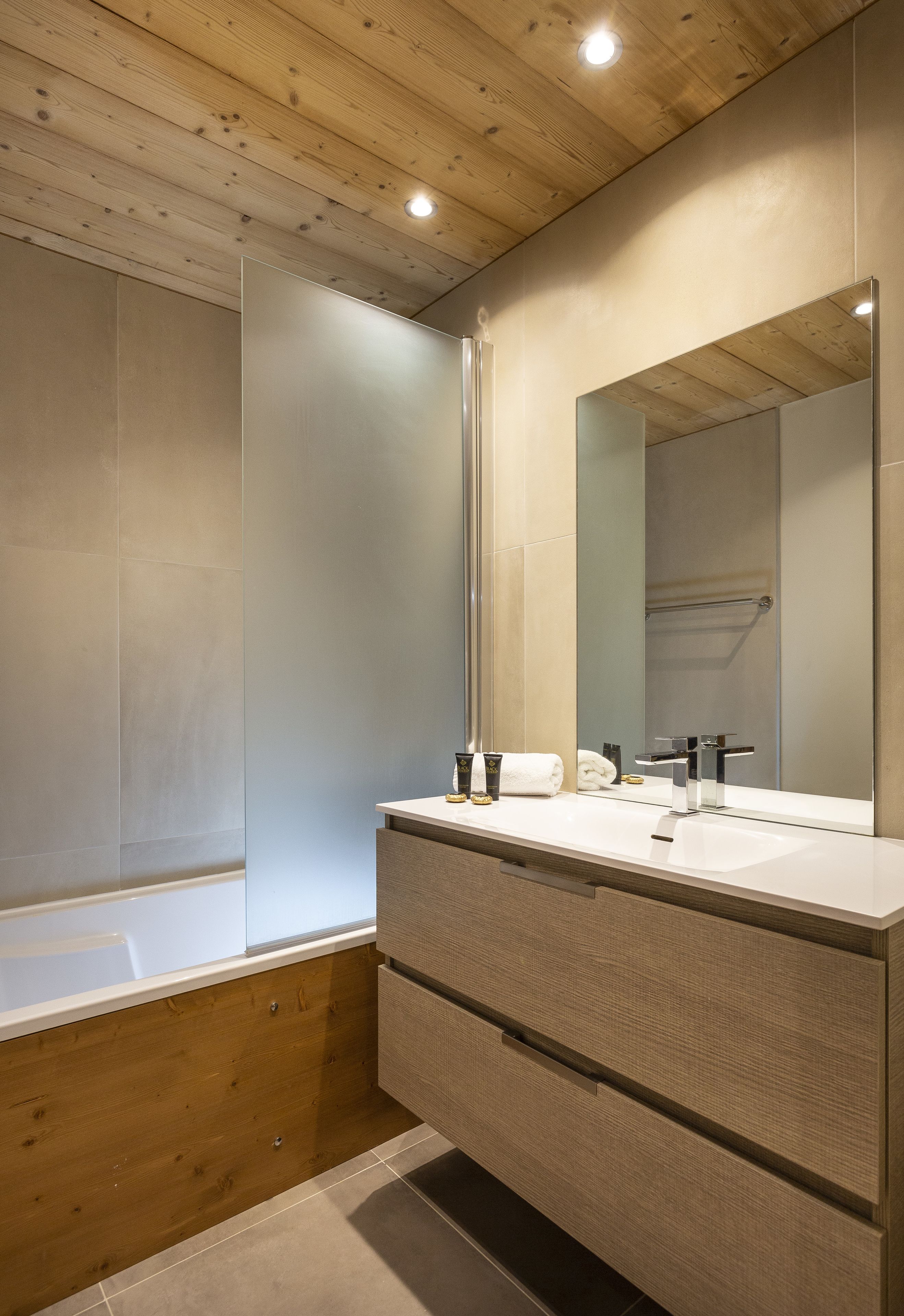 A modern bathroom with a wooden ceiling, a large mirror, a white sink, and a wooden vanity.