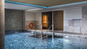 Une piscine intérieure avec un plafond en bois, des murs en pierre et une bouée de sauvetage placée sur le bord.