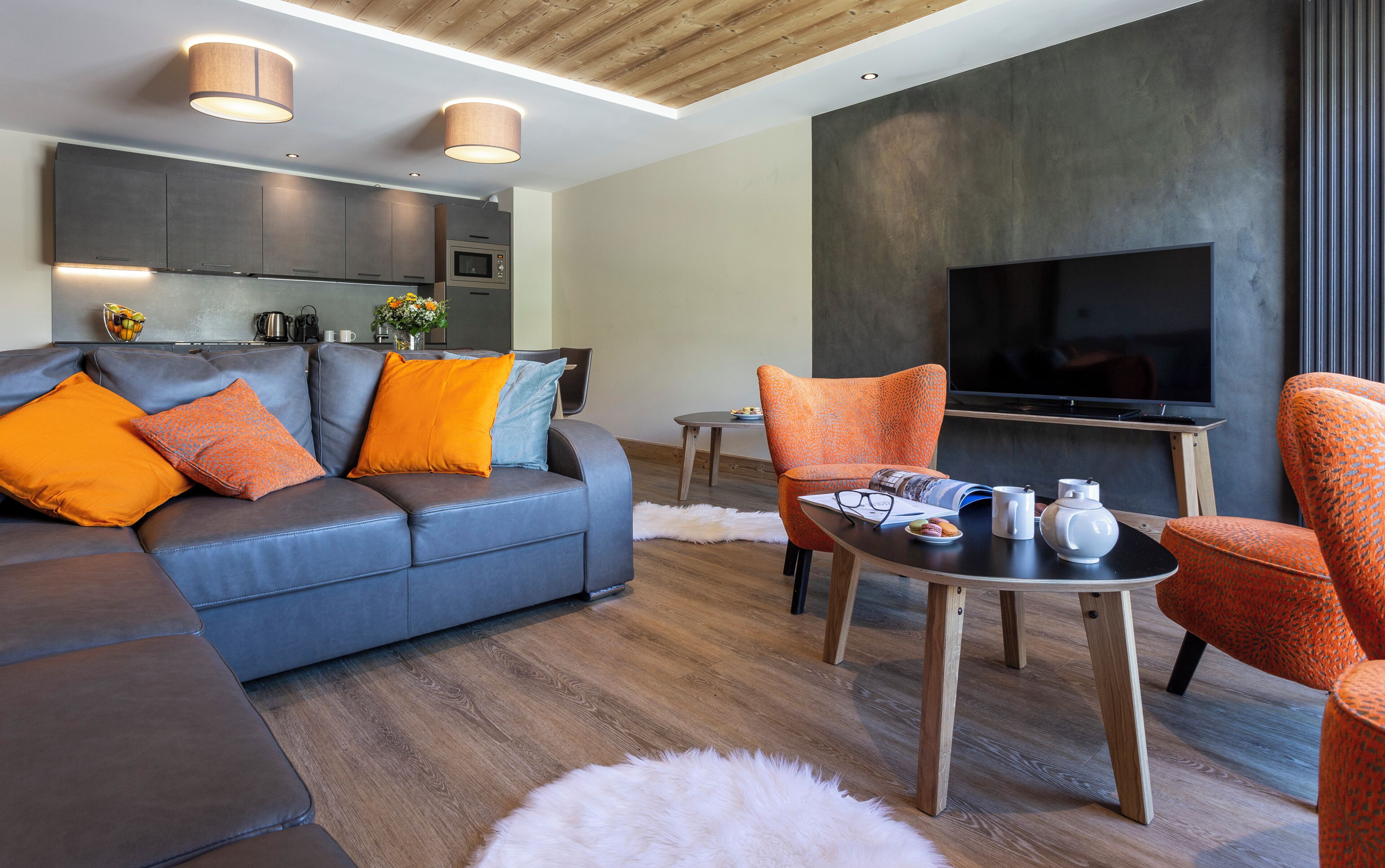 En moderne stue med en grå sofa, orange puder, et sofabord og et fladskærms-tv.
