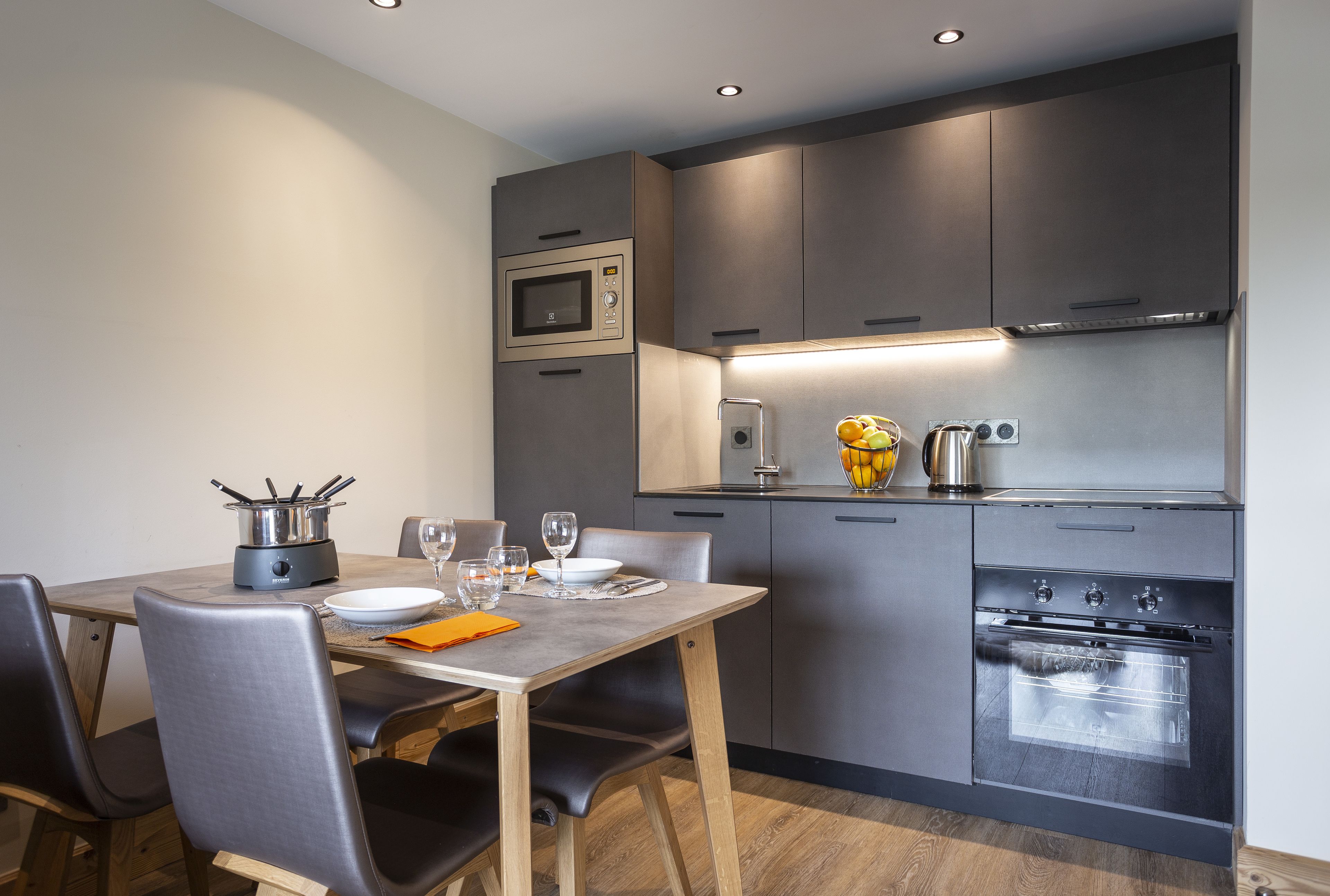 Una cocina moderna con horno empotrado, microondas y un comedor con mesa y sillas.