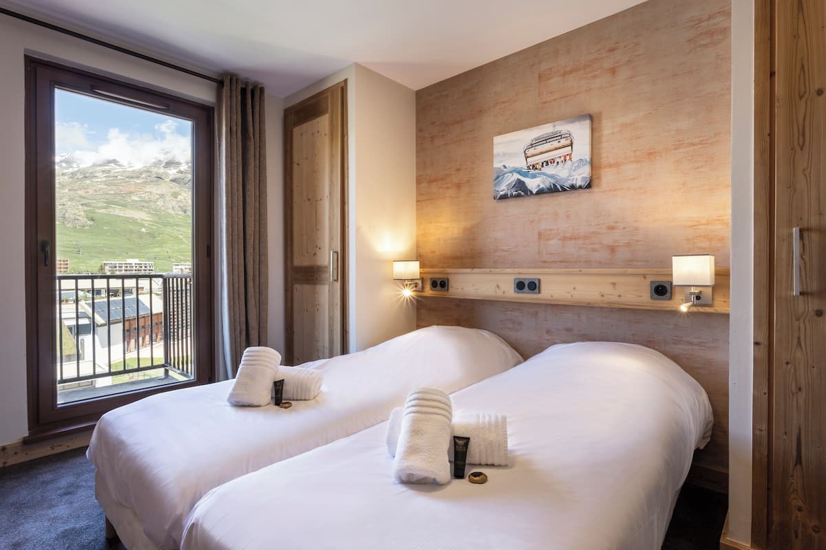 Ein Hotelzimmer mit zwei Betten, einem großen Fenster mit Bergblick und einer Holzwand mit einem Bild.