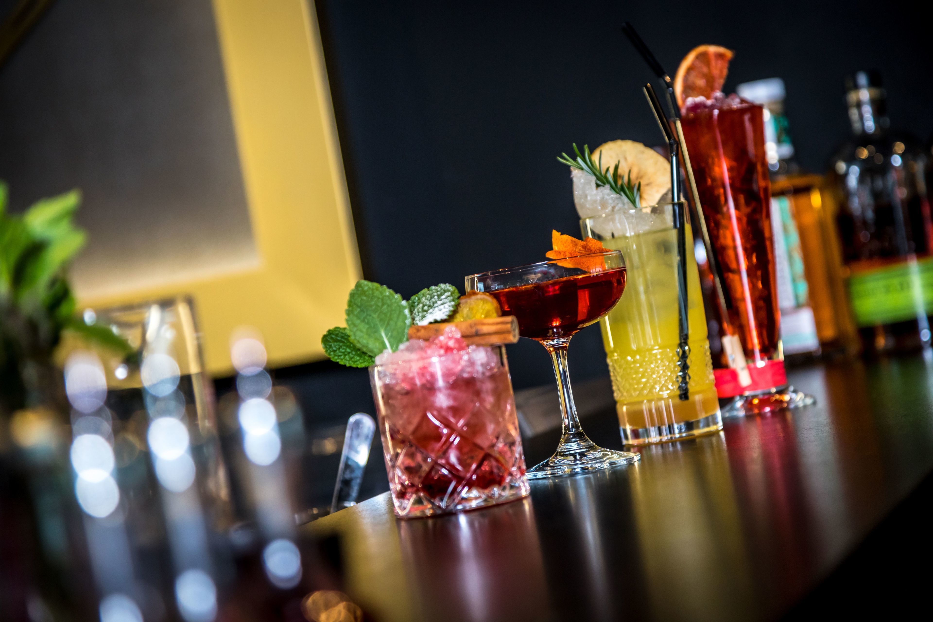 A bar with various cocktails, including a red drink with a garnish and a tall glass with a lime wedge.