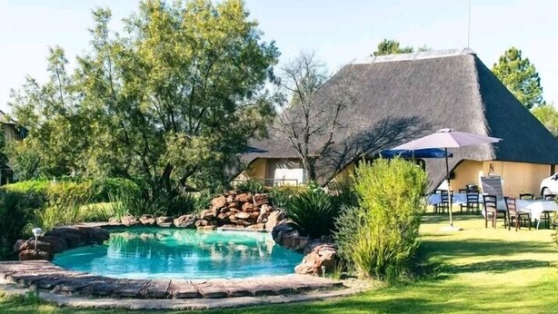 Una piscina con borde de roca natural, rodeada por un césped cuidado y árboles.