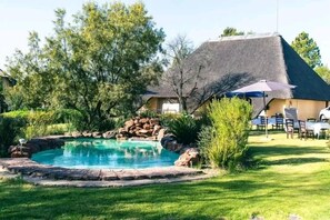 Une piscine bordée de rochers naturels, entourée d’une pelouse bien entretenue et d’arbres.