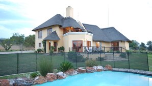 Una casa de dos pisos con piscina, patio cercado y un balcón grande.
