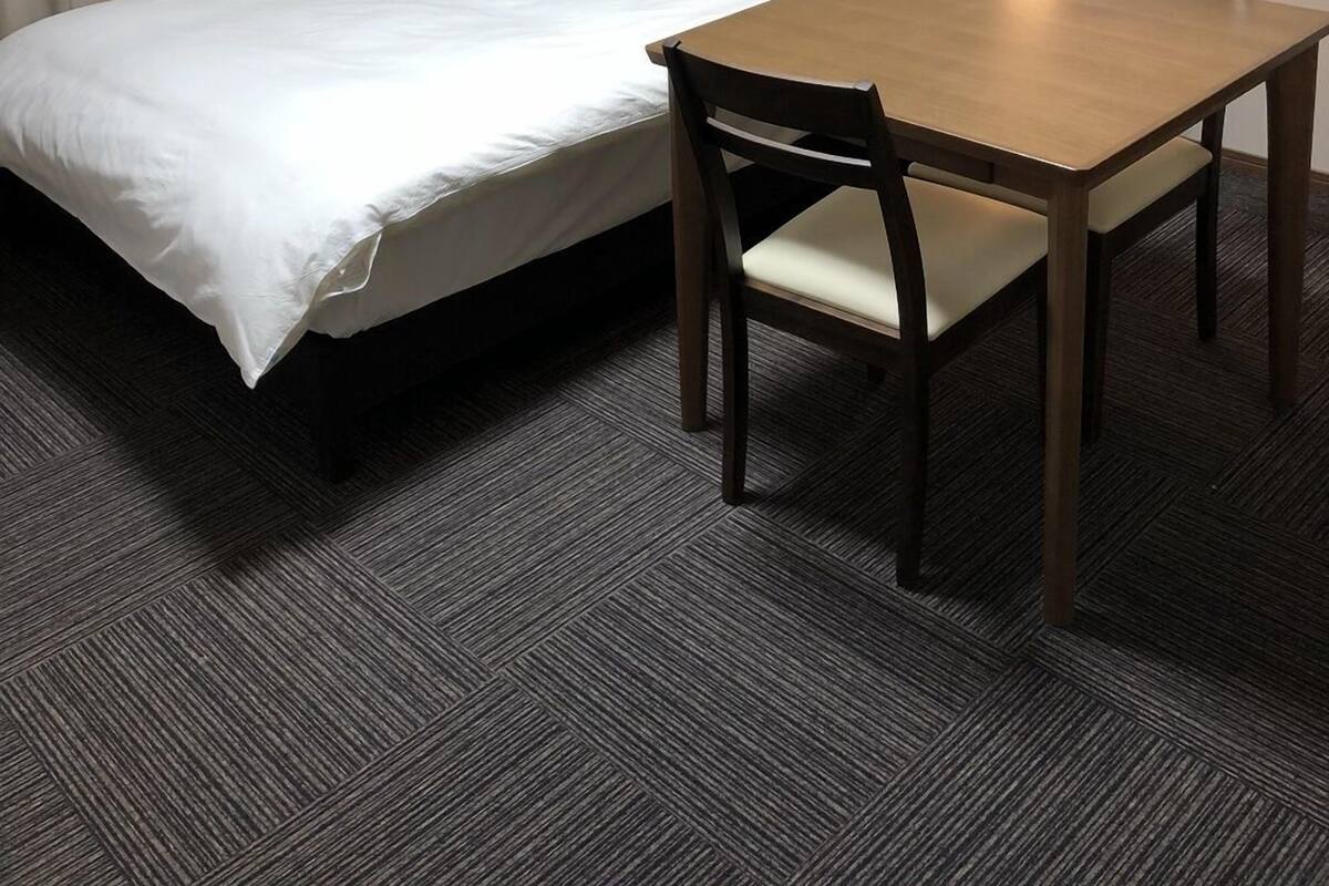 Una cama individual con cabecera de madera, una mesita con una silla y un equipo de aire acondicionado en la pared.