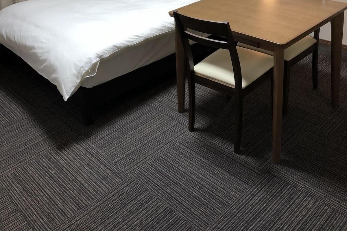 Un lit simple avec une tête de lit en bois, une petite table avec une chaise et un appareil de climatisation fixé au mur.