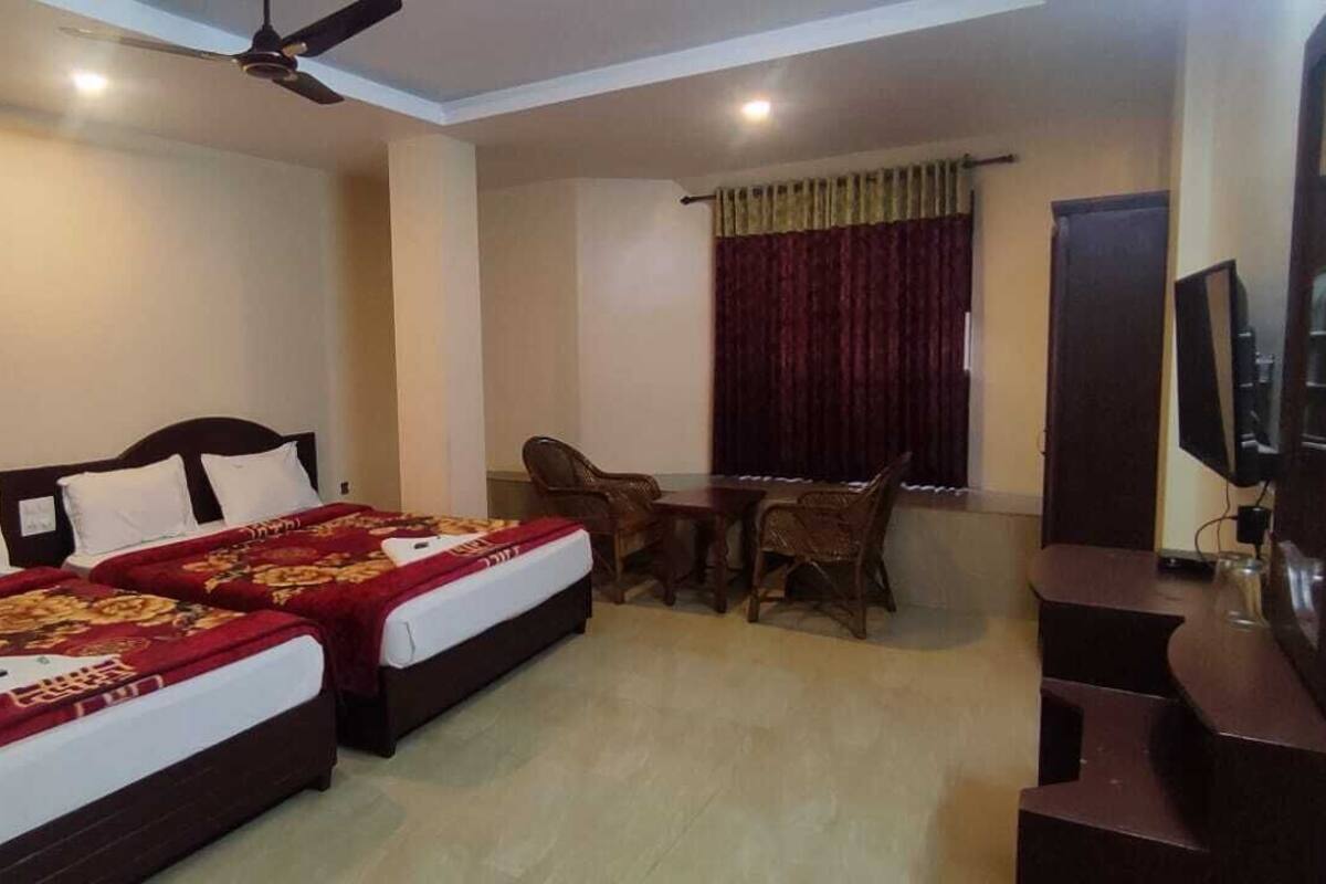 A hotel room with two beds, a dining table with chairs, a television, and a ceiling fan.