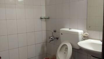 Een badkamer met witte betegelde wanden, een blauw geruit vloertje, een wit toilet, een witte wastafel en een douchekop.
