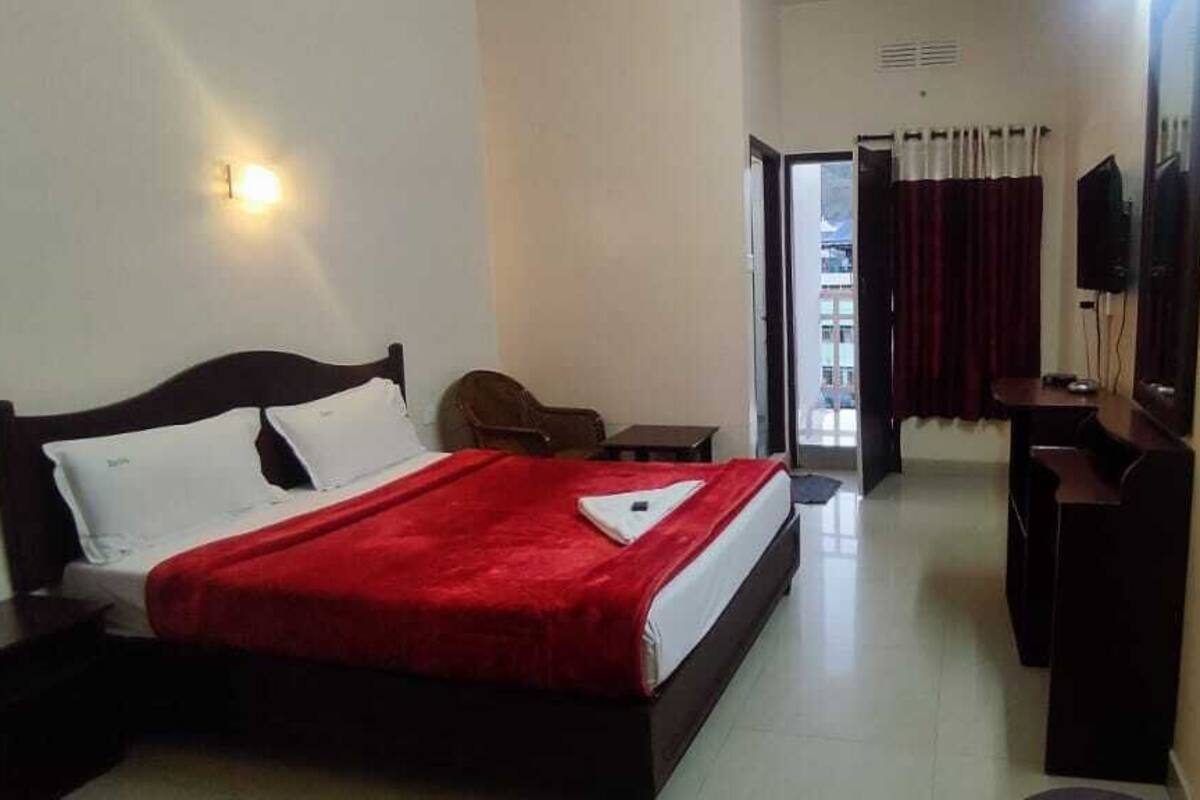 A hotel room with a bed, a desk, a chair, a TV, and a door.