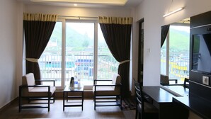 A hotel room with two chairs, a small table, a TV, and a large window with curtains.