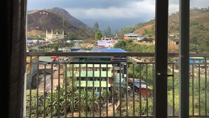 A view from a balcony with a metal railing, overlooking a village with buildings, including a tourist home, and a mountain in the background.